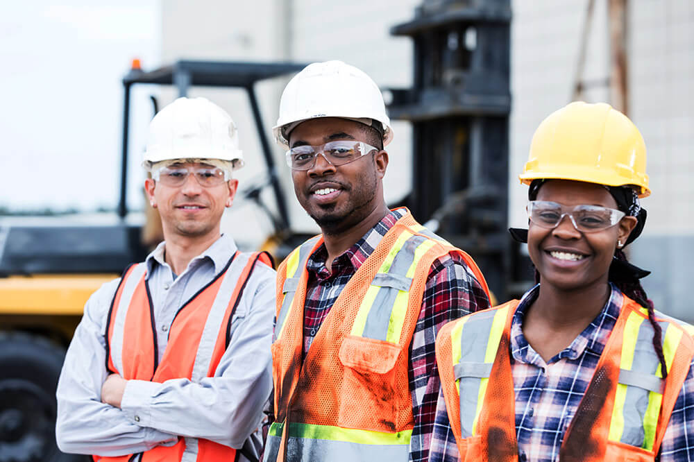 3 construction workers standing next to one another with hardhats on 